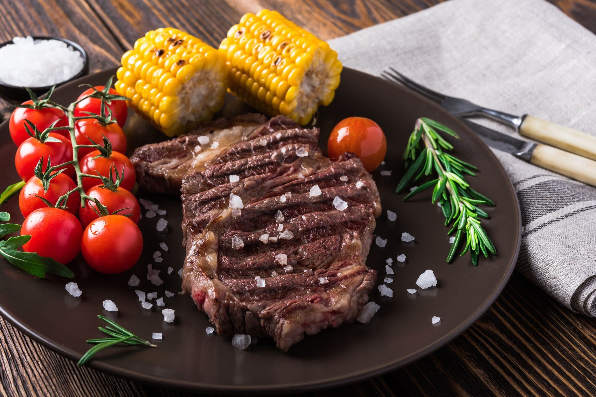 Grilled beef steak ribeye with cherry tomatoes, rosemary and corn on wooden background