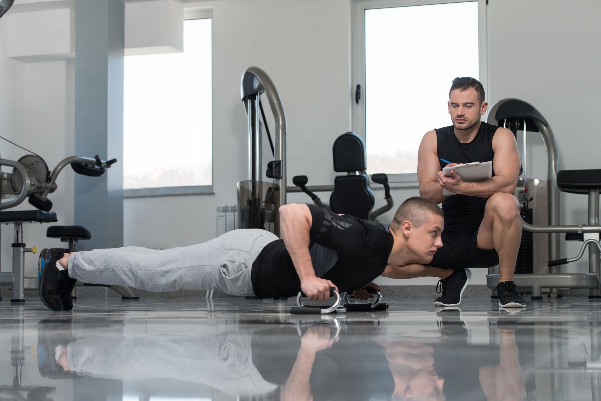 Personal Trainer Showing Young Man How To Exercise Push-Up Strength In A Health And Fitness Concept